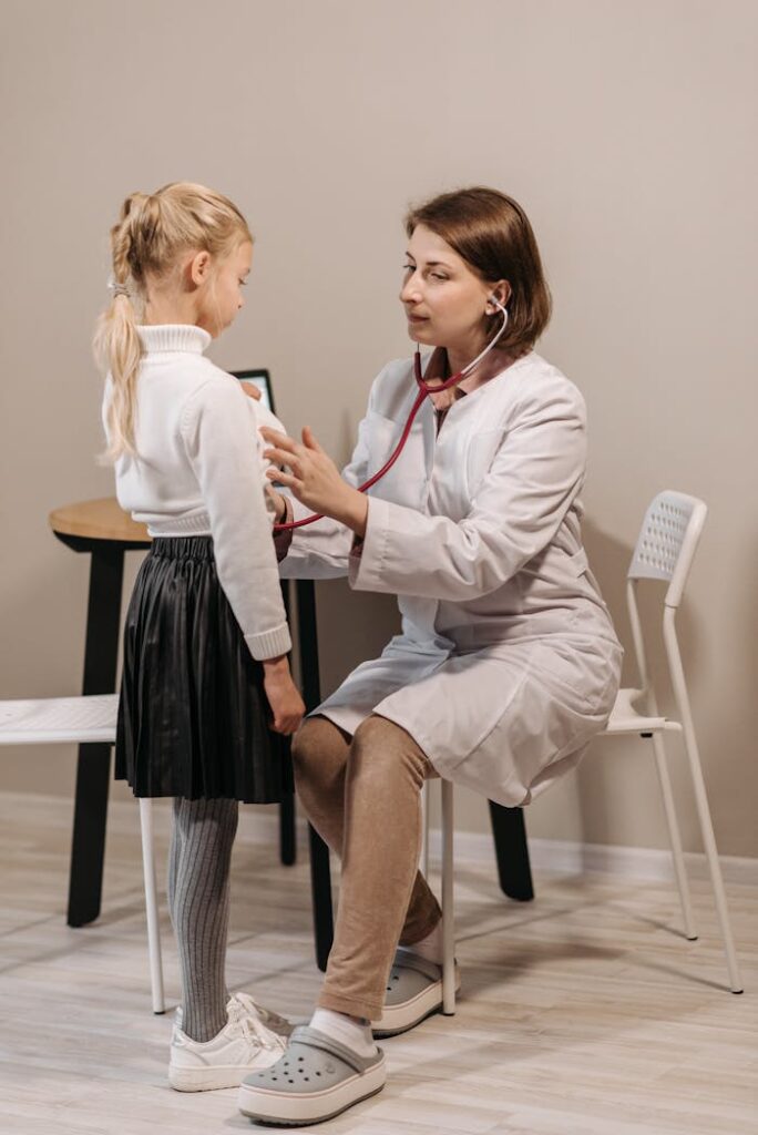 A healthcare worker examining a child with a stethoscope in a clinic setting.